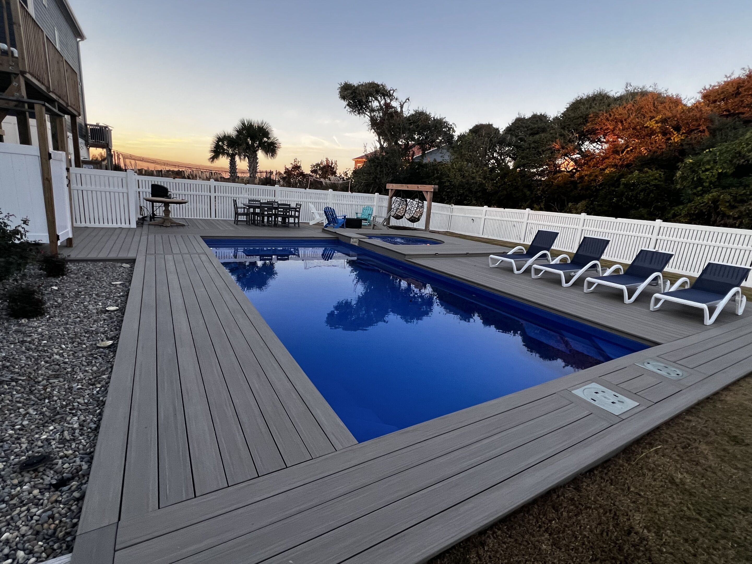 A rectangular swimming pool with a wooden deck, surrounded by a white fence.