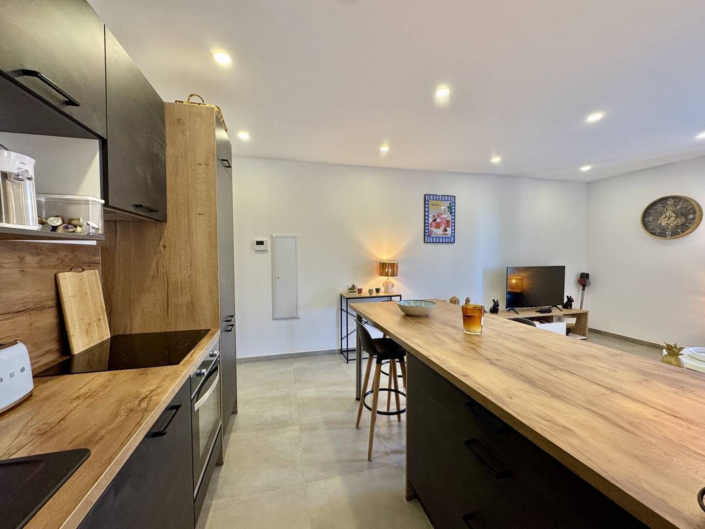 Cocina moderna con una isla de madera, electrodomésticos integrados y una zona de comedor con televisor y asientos.