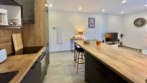 A modern kitchen with a wooden island, built-in appliances, and a dining area with a TV and seating. - Magnifique T3 tout confort (PROPRIANO)