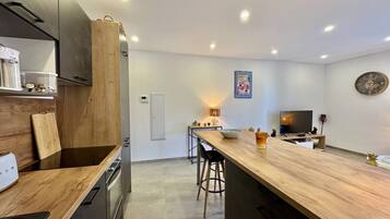 Cocina moderna con una isla de madera, electrodomésticos integrados y una zona de comedor con televisor y asientos.
