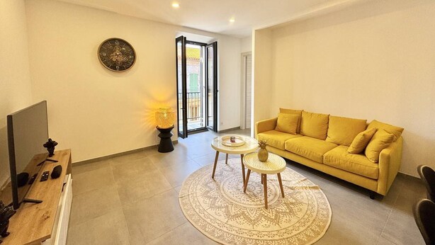 A living room with a yellow sofa, a round coffee table, a TV, and a patterned rug. - Magnifique T3 tout confort (PROPRIANO)