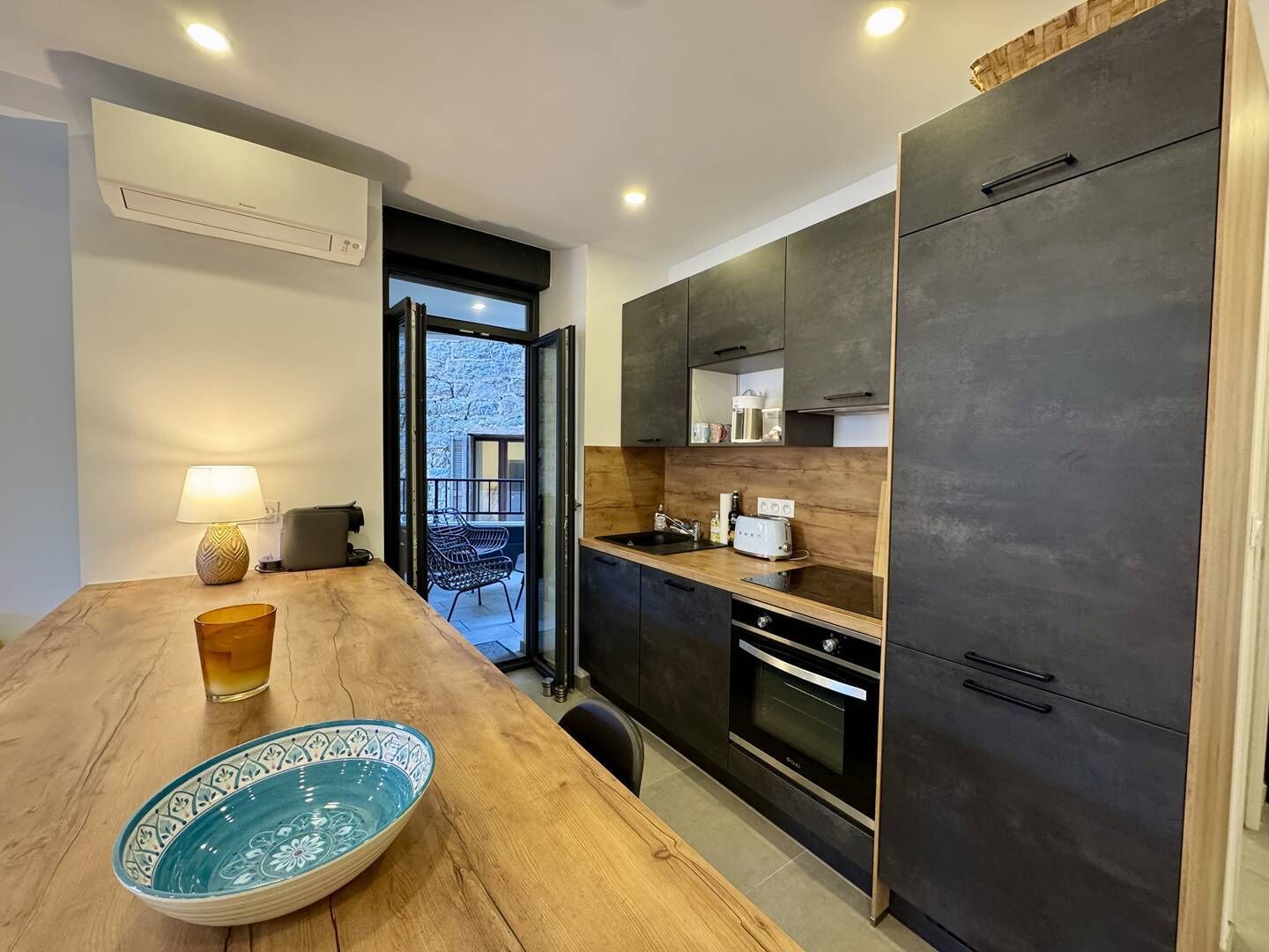 Una cocina moderna con armarios oscuros, encimera de madera y zona de comedor con mesa y sillas.