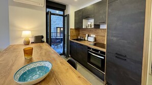 A modern kitchen with dark cabinets, a wooden countertop, and a dining area with a table and chairs. - Magnifique T3 tout confort (PROPRIANO)