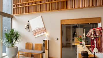 A modern interior with a wooden slatted ceiling, a bench, a wall-mounted lamp, and a decorative wall hanging.