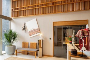 A modern interior with a wooden slatted ceiling, a bench, a wall-mounted lamp, and a decorative wall hanging. - Na U Hotel (Chiang Mai)