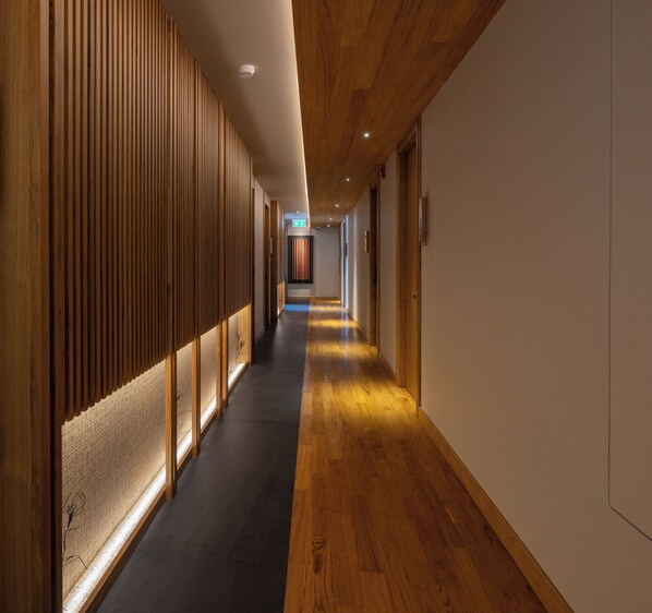 A long, narrow hallway with wooden paneling on one side and a carpeted floor. - Na U Hotel (Chiang Mai)