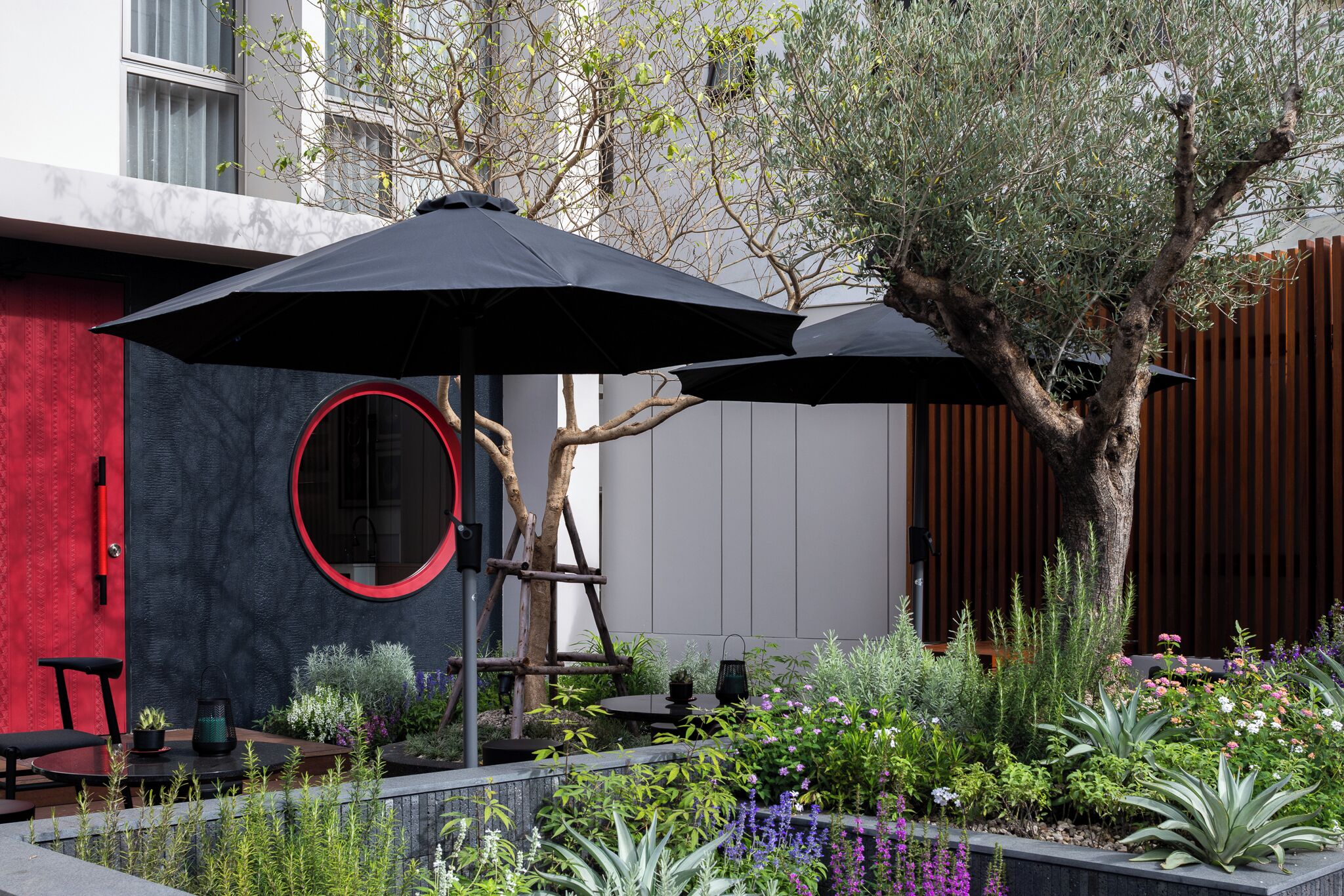 A modern outdoor seating area with a circular mirror, black umbrellas, and a variety of plants.