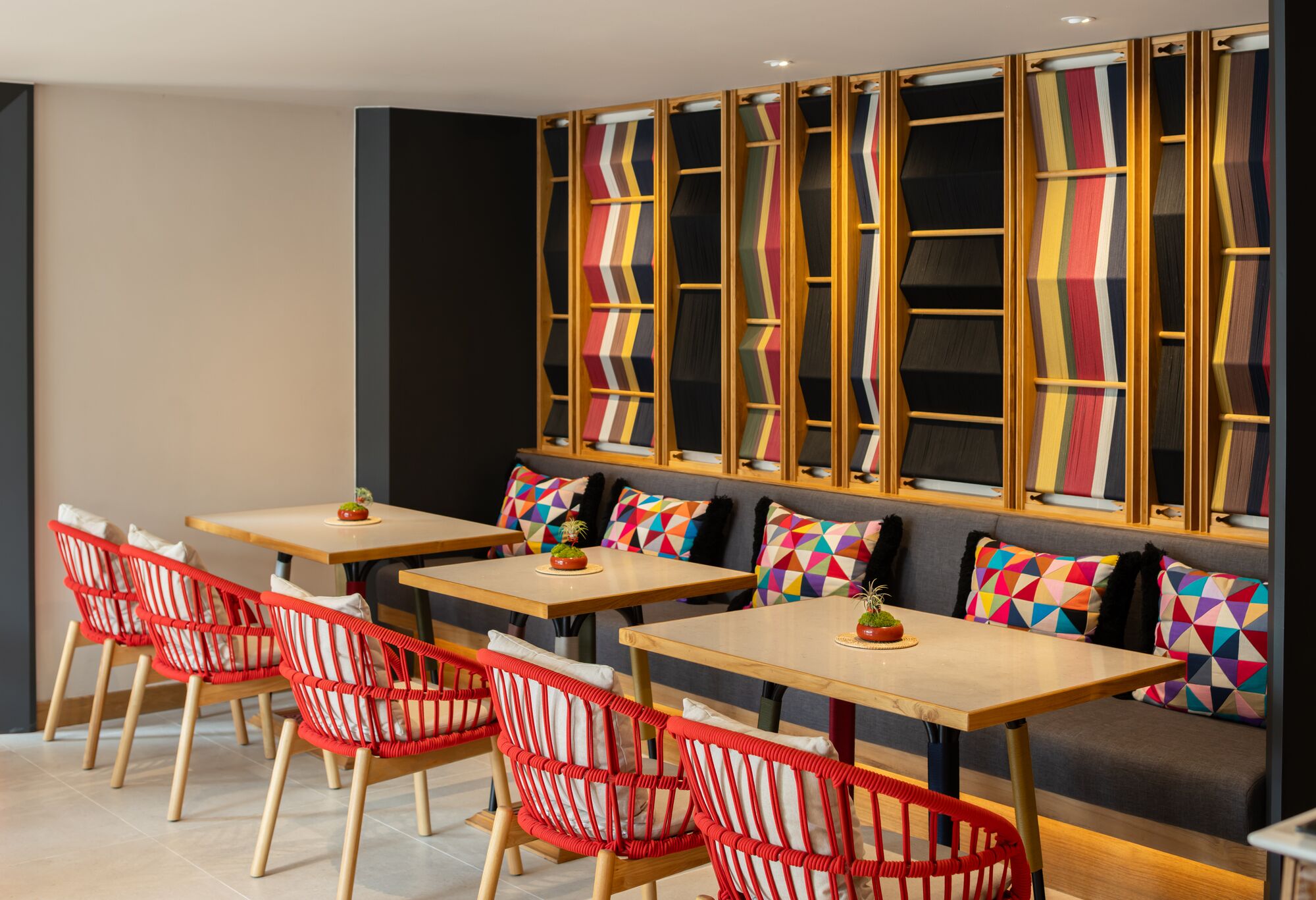 Un interior moderno con una zona de estar que incluye sillas rojas y un sofá con cojines geométricos de colores.