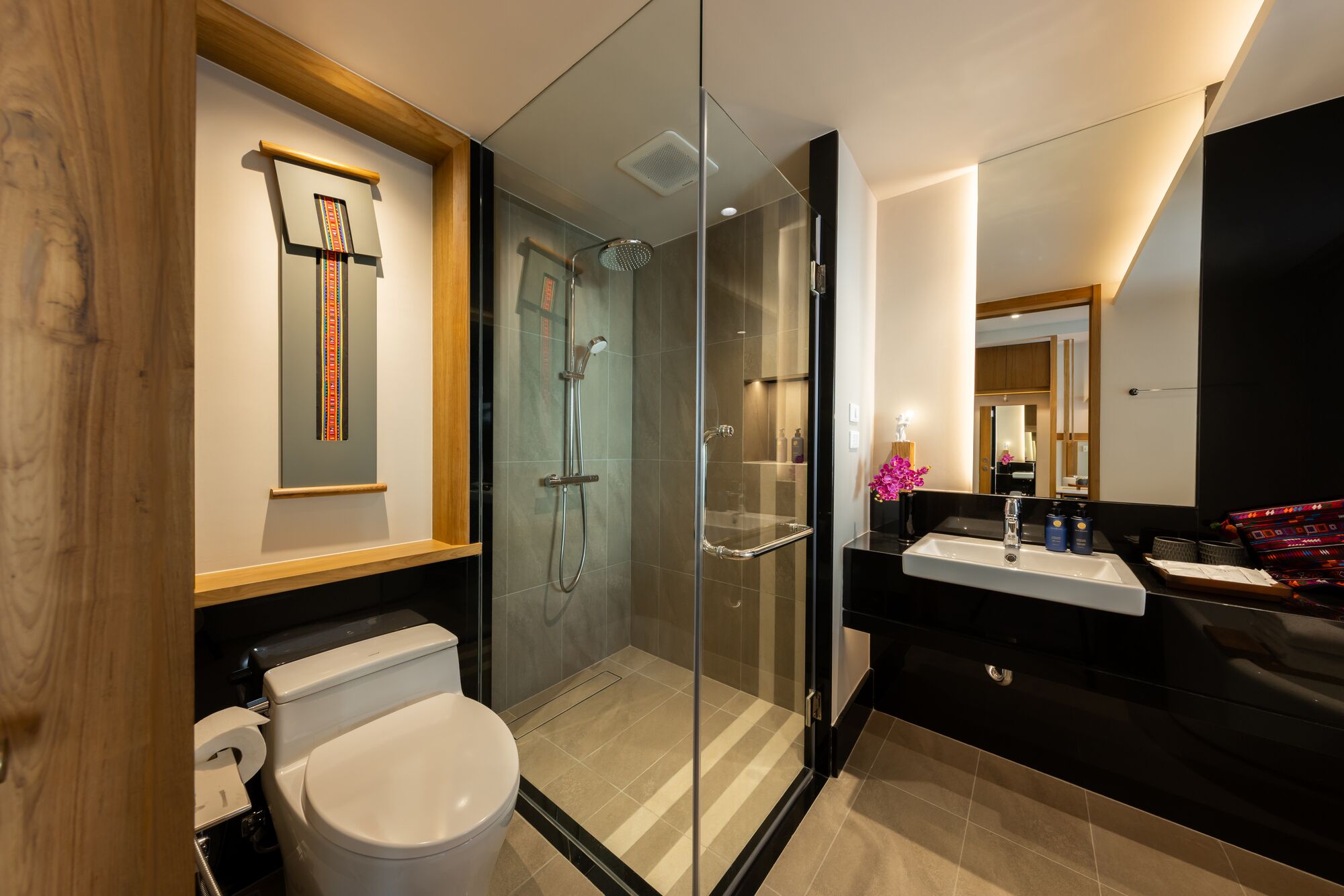 A modern bathroom with a glass-enclosed shower, a toilet, and a vanity with a mirror.