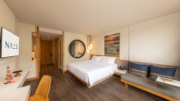 A hotel room with a bed, a sofa, a desk, and a mirror.