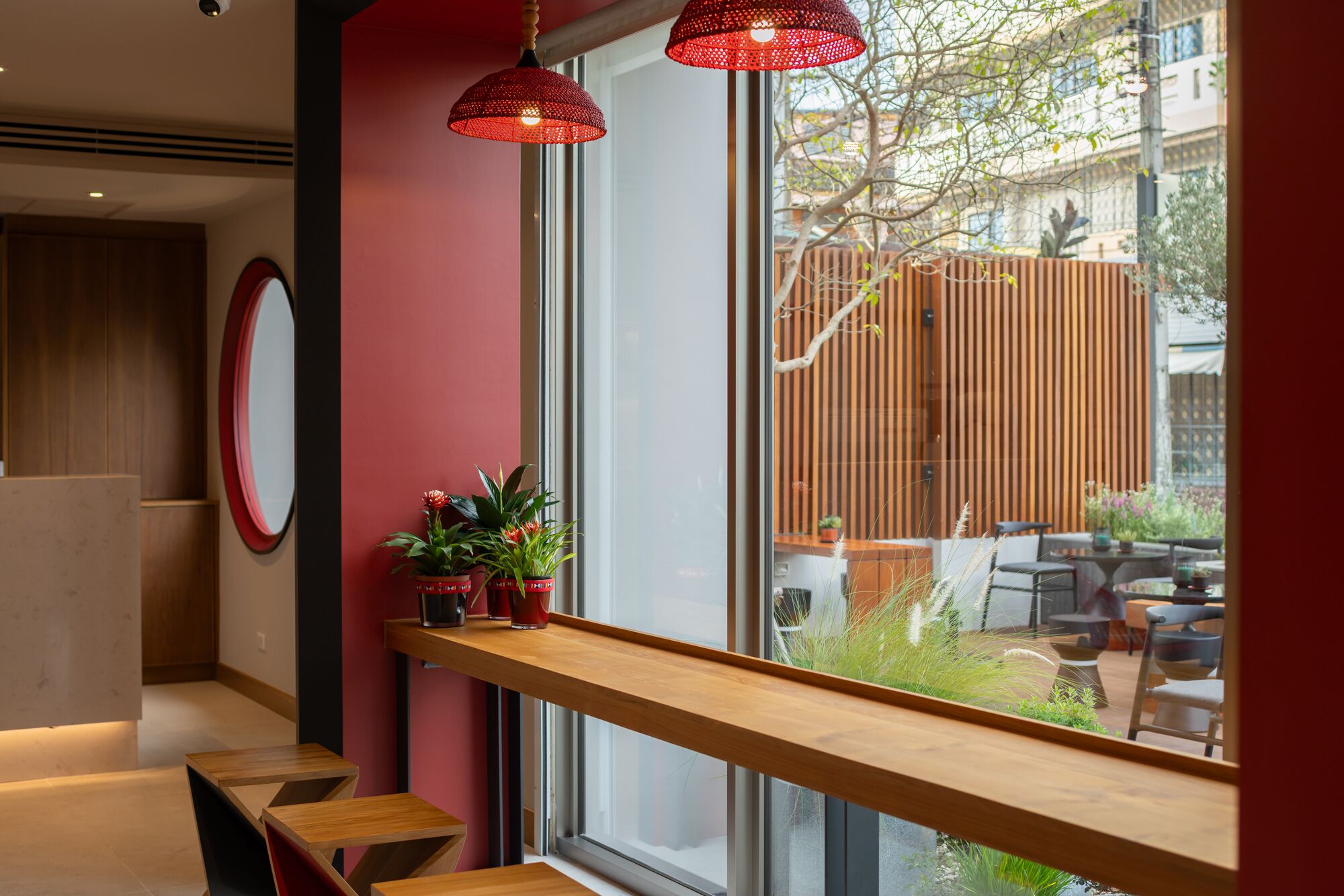 A modern interior with a wooden bench, a red wall, and a window overlooking a garden.