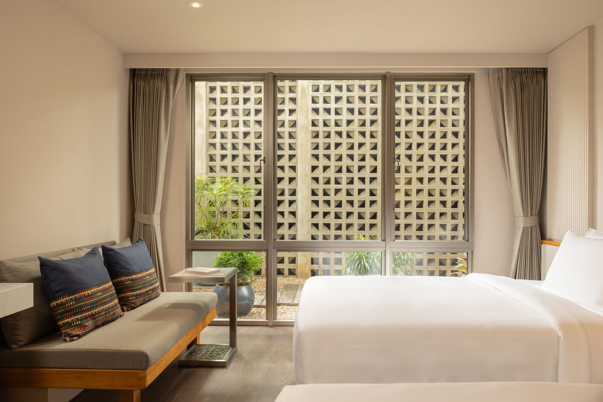 A hotel room with a bed, a sofa, a small table, and a view through a window with a lattice screen.