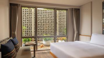 A hotel room with a large bed, a seating area with cushions, a small table, and a view through a window with a lattice screen.