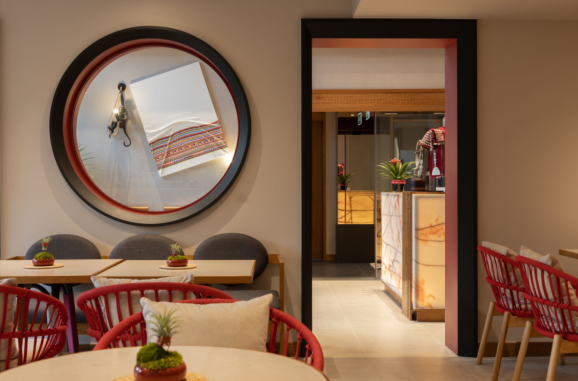 A modern interior with a round mirror, red wicker chairs, and a dining area.