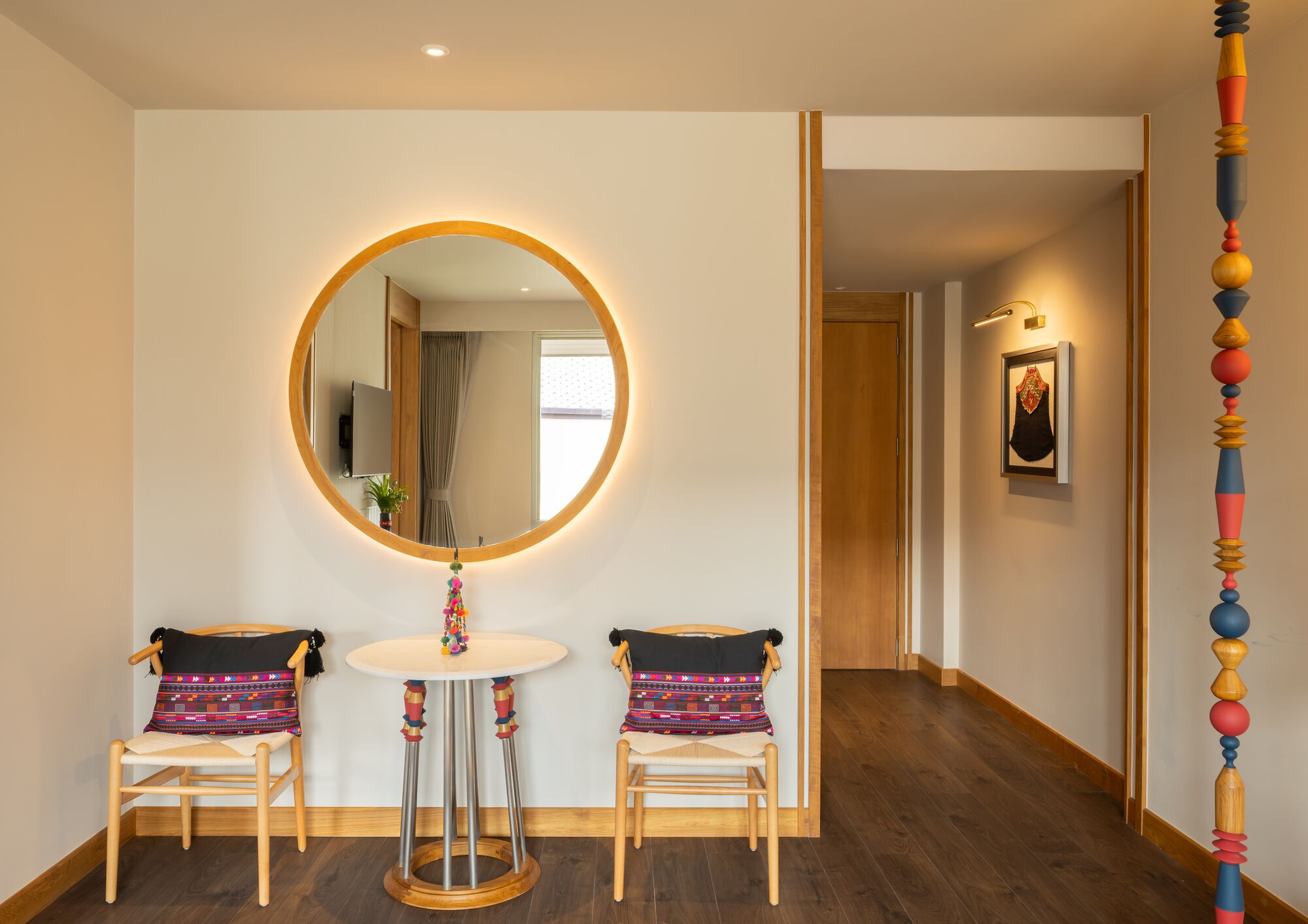 Una habitación con un espejo redondo, dos sillas, una mesita y suelo de madera.