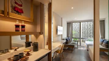 A modern hotel room with a kitchen area, a dining table, a sofa, and a large window with a view.