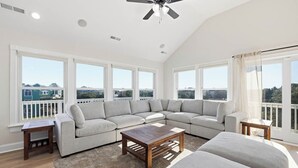 Ein großzügiges Wohnzimmer mit einer großen Eckcouch, einem Holztisch und einem Deckenventilator.