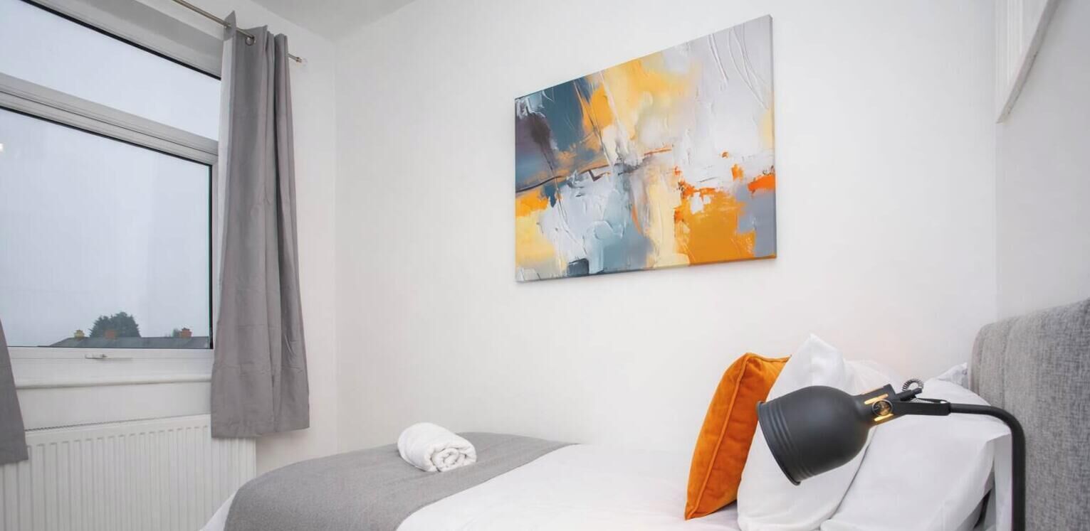 Ein Hotelzimmer mit Bett, einem Fenster mit Vorhängen, einem Bild an der Wand und einer Lampe auf dem Nachttisch.