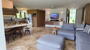 Ein modernes Wohnzimmer mit einem grauen Sofa, einem kleinen Hocker und einem an der Wand befestigten Fernseher.