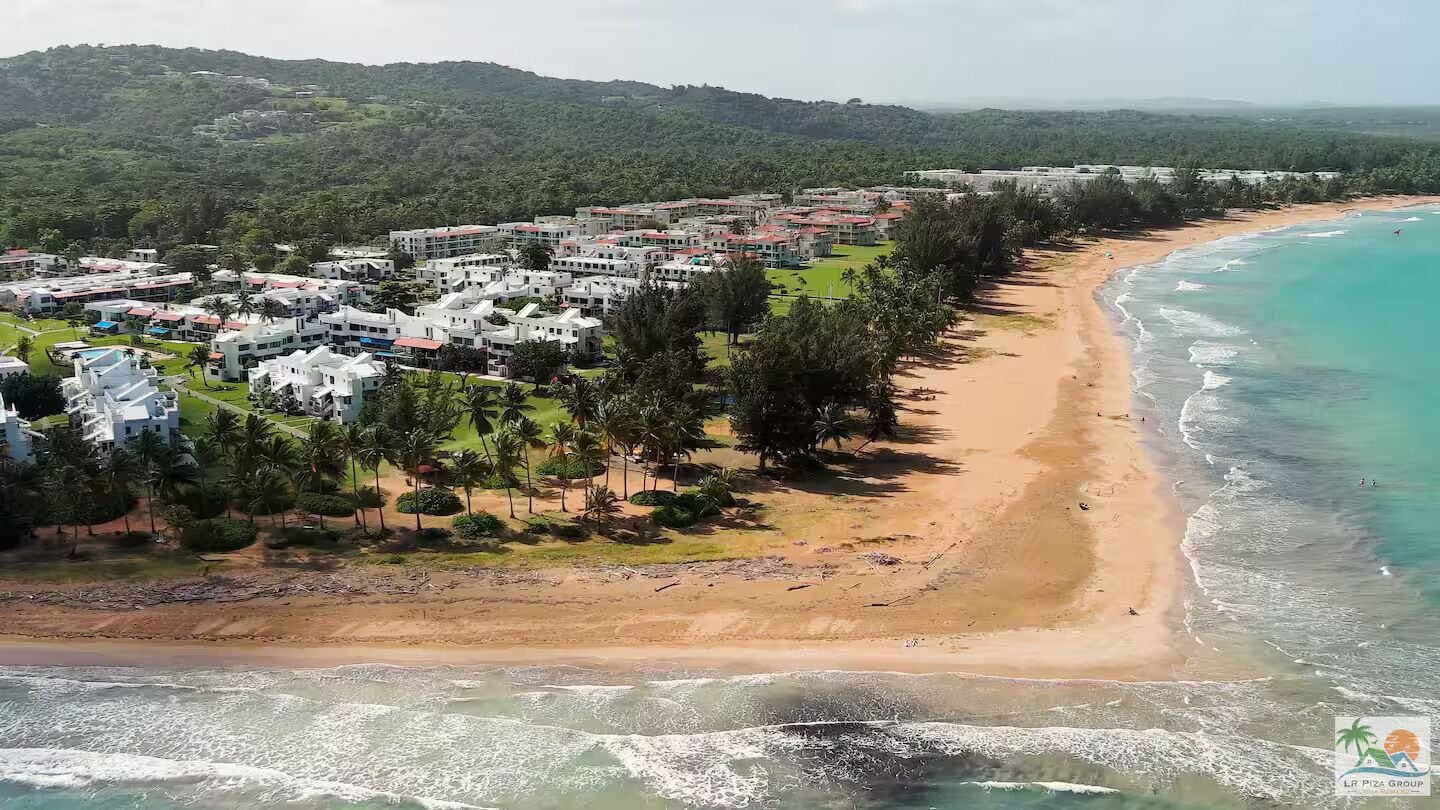 An aerial view of a coastal resort with beachfront villas, a sandy beach, and a view of the ocean.