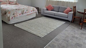 Un dormitorio con cama, sofá, sillón, alfombra y ventana con cortinas.