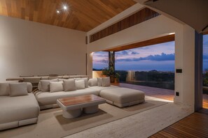 Ein modernes Wohnzimmer mit einem Ecksofa, einem Couchtisch und einem großen Fenster mit Blick ins Freie.