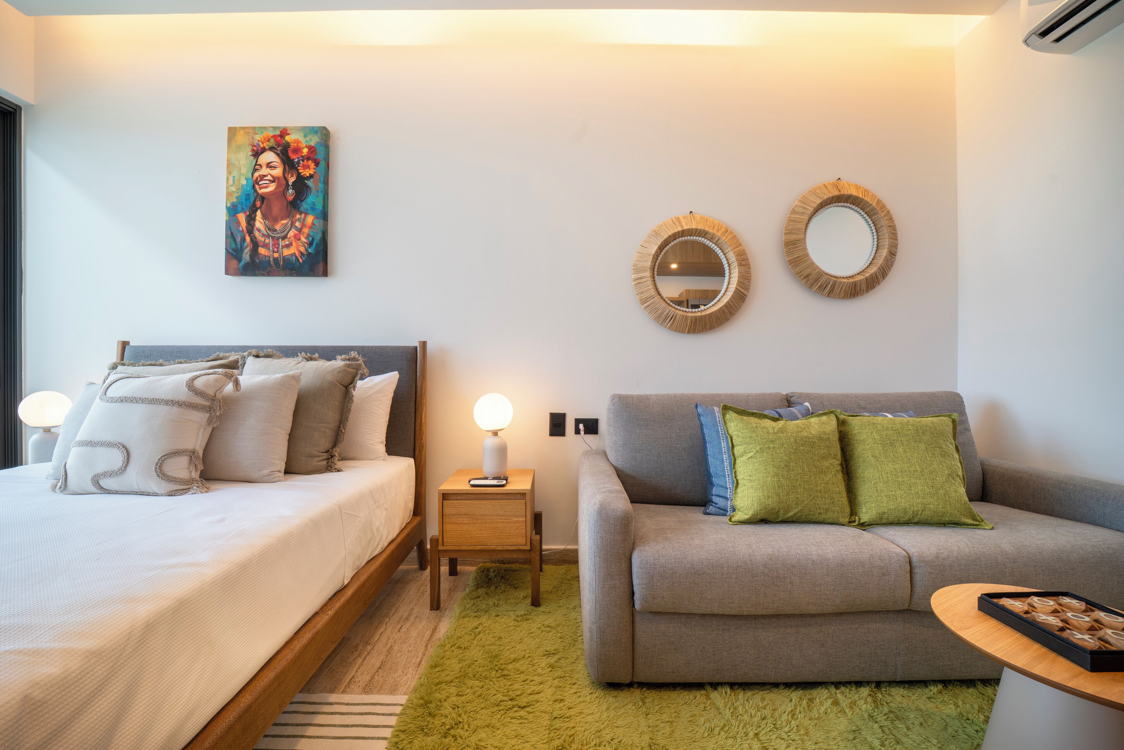 Een slaapkamer met een bed, een grijze bank, twee spiegelwanden en een schilderij.