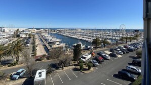 Un port de plaisance où sont amarrés de nombreux bateaux, un parking rempli de voitures et, au loin, une grande roue.