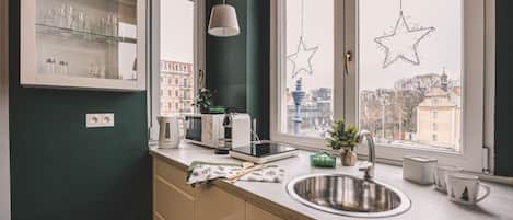 A modern kitchen with a built-in microwave, toaster, and kettle, a window with star decorations, and a view of buildings outside.