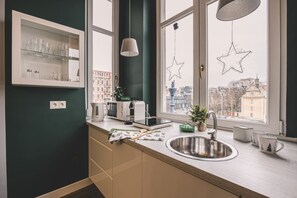 A modern kitchen with a built-in microwave, toaster, and kettle, a window with star decorations, and a view of buildings outside. - Botella Kr Lewskie Studio w Sercu Poznania (Poznań)