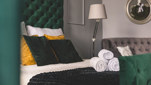 A neatly made bed with rolled towels, a lamp, and a wall-mounted mirror in a hotel room. - Botella Kr Lewskie Studio w Sercu Poznania (Poznań)