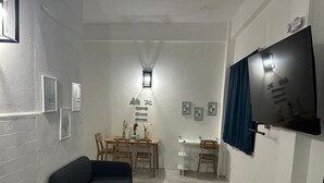Una camera funzionale con un letto, un divano letto, un tavolo da pranzo con sedie, una TV a parete e alcune foto incorniciate.