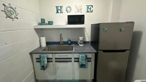 Una cucina compatta con lavandino, forno a microonde, frigorifero e un cartello con la scritta 'HOME'.