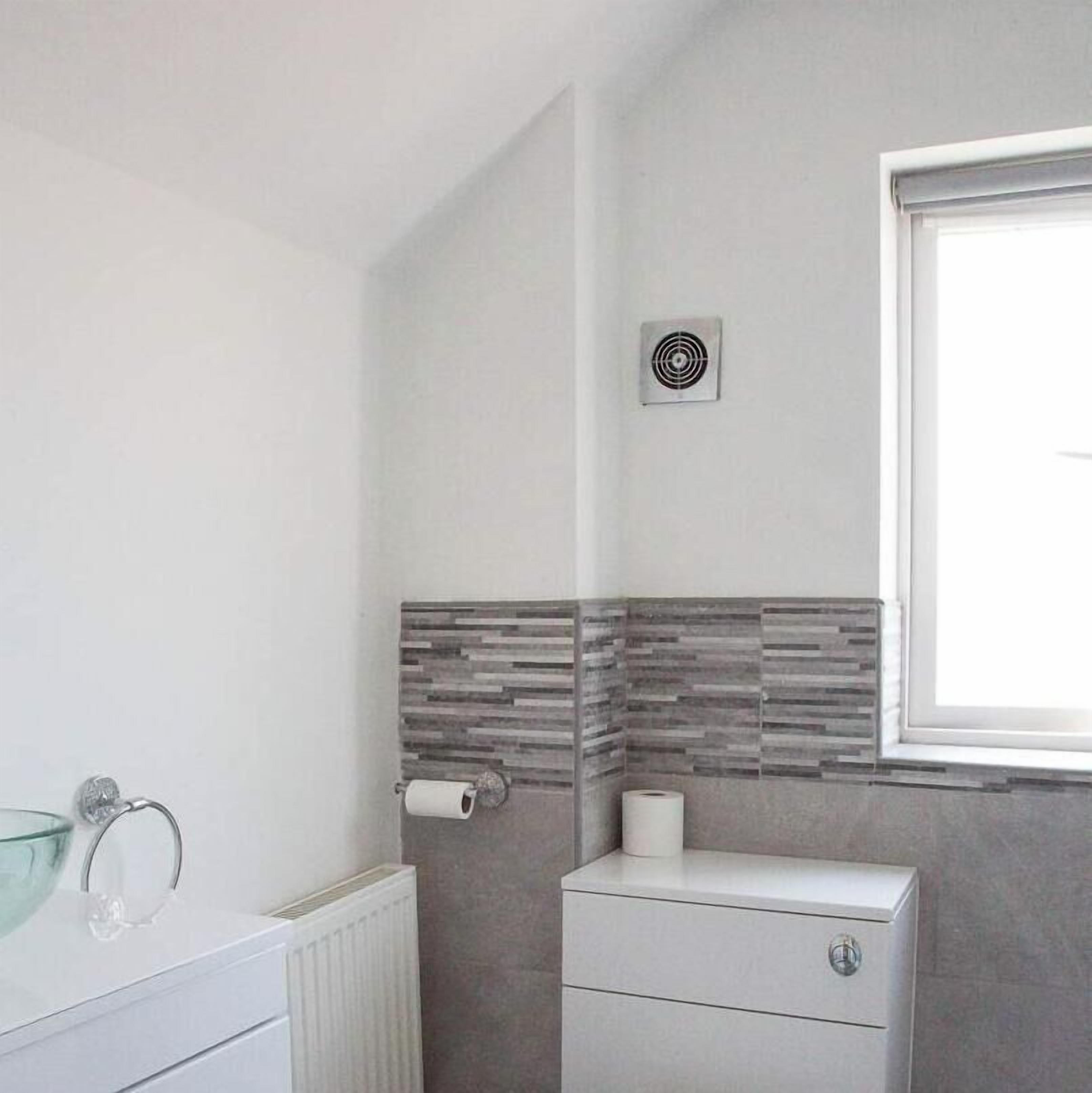 A bathroom with a white radiator, a toilet with a roll of toilet paper, and a window with a white blind.