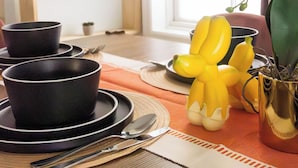 A dining table set with black bowls, plates, and cutlery, accompanied by a yellow decorative item and a potted plant. - Projector - 5 mins to DT - 4 King Beds - Massage Chair (Savannah)