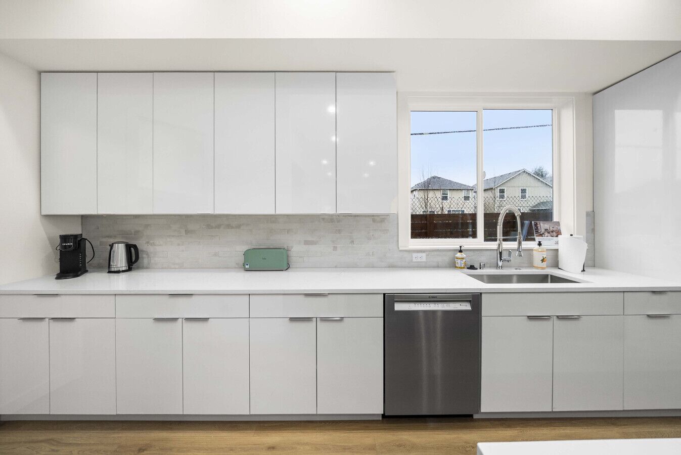 Una cocina moderna con armarios blancos, lavavajillas de acero inoxidable y ventana con vistas a casas.