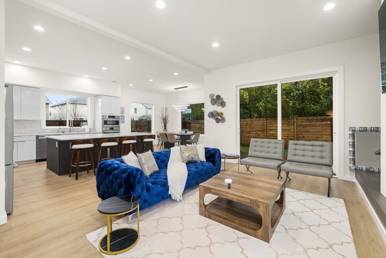 A modern kitchen with white cabinets and a dining area with a blue sofa and grey chairs.
