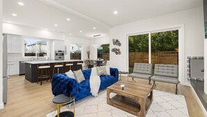 A modern kitchen with white cabinets and a dining area with a blue sofa and grey chairs. - Brand New 5BR Home Fenced Yard Ample Parking (Renton)