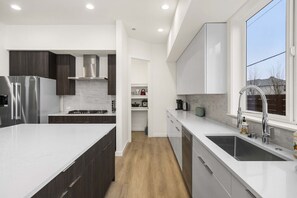 Una cucina moderna con mobili in legno scuro, ripiani bianchi, un frigorifero in acciaio inox, un piano cottura a gas e una finestra con vista esterna.