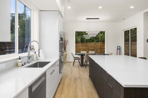 Una cucina moderna con una grande isola, elettrodomestici integrati e un'area pranzo con vista sull'esterno.