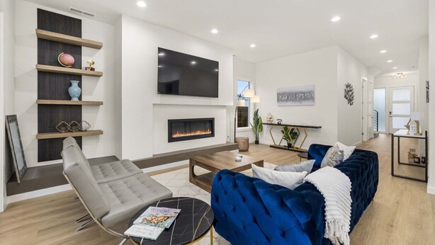 A modern living room with a fireplace, a large flat-screen TV, and a blue sofa. - Brand New 5BR Home Fenced Yard Ample Parking (Renton)