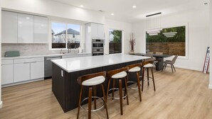 A modern kitchen with a large island, bar stools, and a dining area with a view of the outdoors. - Brand New 5BR Home Fenced Yard Ample Parking (Renton)