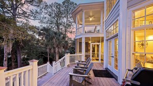 Une terrasse en bois, dotée de chaises Adirondack et d’un barbecue, entourée d’arbres.