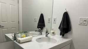 Een badkamer met een witte wastafel, een spiegel en een handdoekhouder. Op het aanrecht van de wastafel staat een mandje met toiletartikelen.