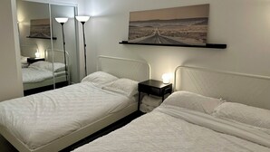 Een hotelkamer met twee bedden, een grote spiegel, een schilderij van een weg en een nachtkastje met een lamp.