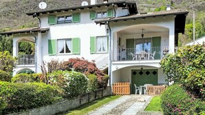 Ein zweistöckiges Haus mit Balkon, umgeben von üppiger Vegetation und einer Bergkulisse.