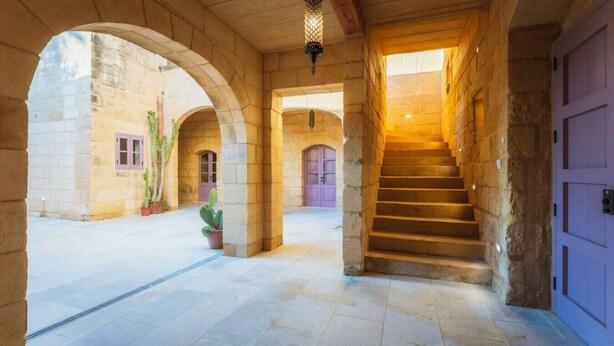A stone corridor with arches, a staircase, and potted plants. - San Lawrenz Farmhouse Rustic Retreat With Pool (San Lawrenz)