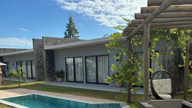 A modern outdoor pool area with a stone wall, a pergola with a swing chair, and wicker furniture. - Casa Milagres Reserva do toque (São Miguel dos Milagres)