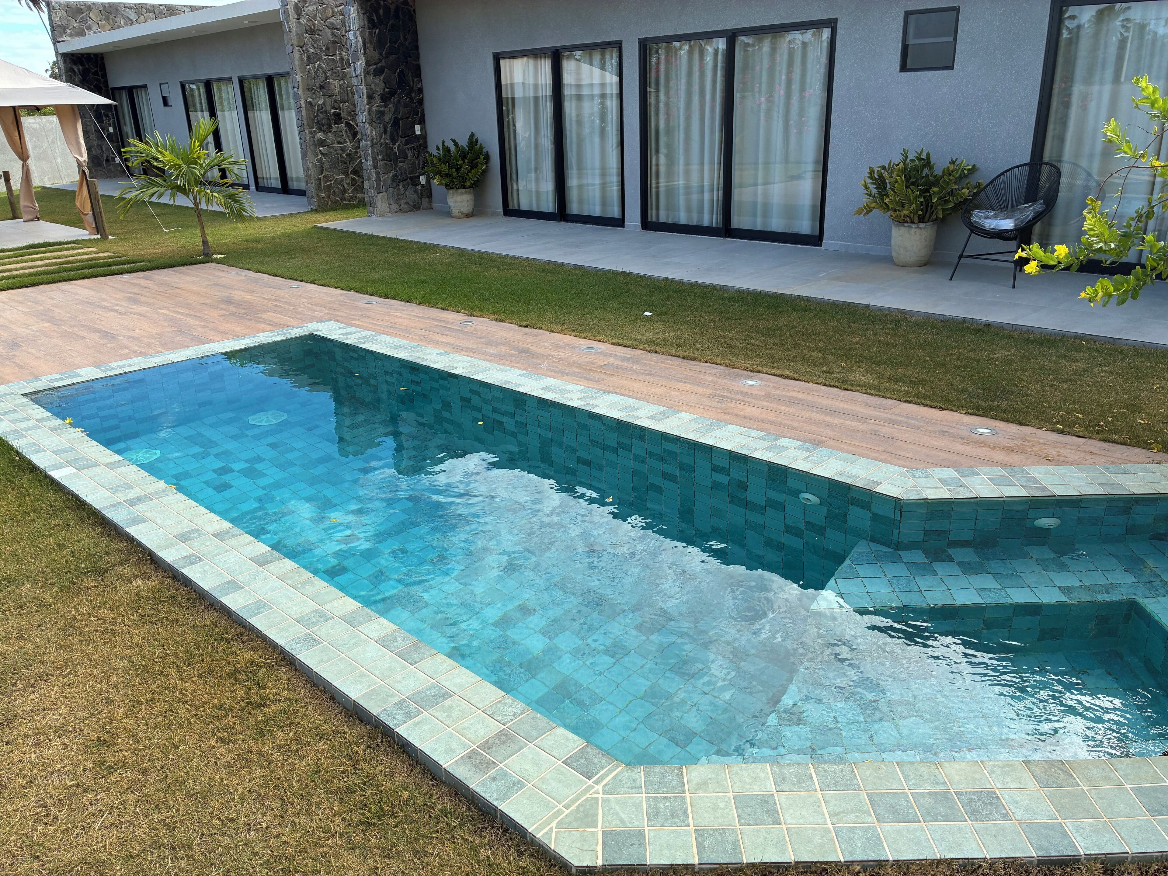 Ein rechteckiger Pool mit einer gefliesten Kante, umgeben von einer Rasenfläche und einer gepflasterten Terrasse.