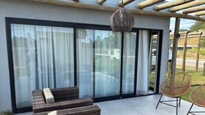 A modern outdoor seating area with wicker furniture, a hanging basket, and a glass door leading to a patio. - Casa Milagres Reserva do toque (São Miguel dos Milagres)